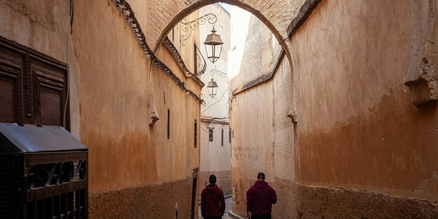 Two people walking under an arch in a narrow medina lane